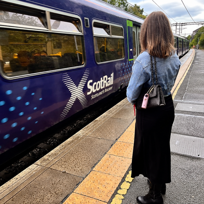 Woman carrying a pink My Robin personal safety alarm on her bag at a train station